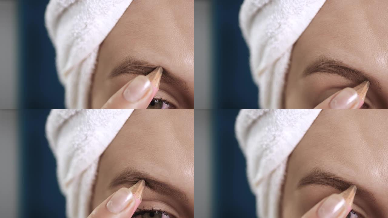 女孩画眉毛。微距拍摄的脸有吸引力的女人与毛巾在蓝色的背景油漆眉毛与特殊的铅笔。化妆师，美容，洁面，化
