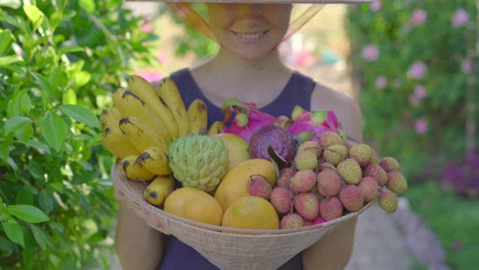 越南帽子里的各种水果。戴越南帽子的女人拿着另一顶装满热带水果的帽子