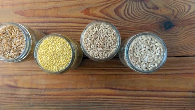 木制背景4k视频玻璃罐中的谷物。收集不同的粒顶视图大麦，燕麦，小米和小麦。全麦食品高纤维含量平铺。健