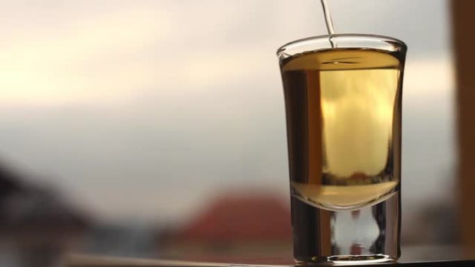 在模糊的晴天背景下，强力的酒精饮料倒入短玻璃杯中。酗酒作为社会问题的概念镜头。