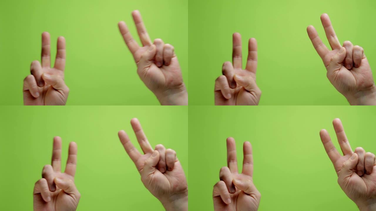 手是符号。男人的手在绿色背景上显示出和平与胜利的姿态