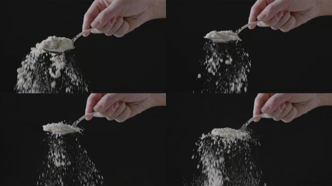 女人的手握着面粉和面粉的勺子，放在黑色的背面