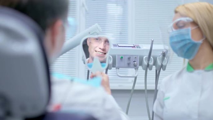 男人看着牙镜，欣赏他的微笑，美丽的直齿。满意的病人看着牙医的镜子，结束牙科治疗。