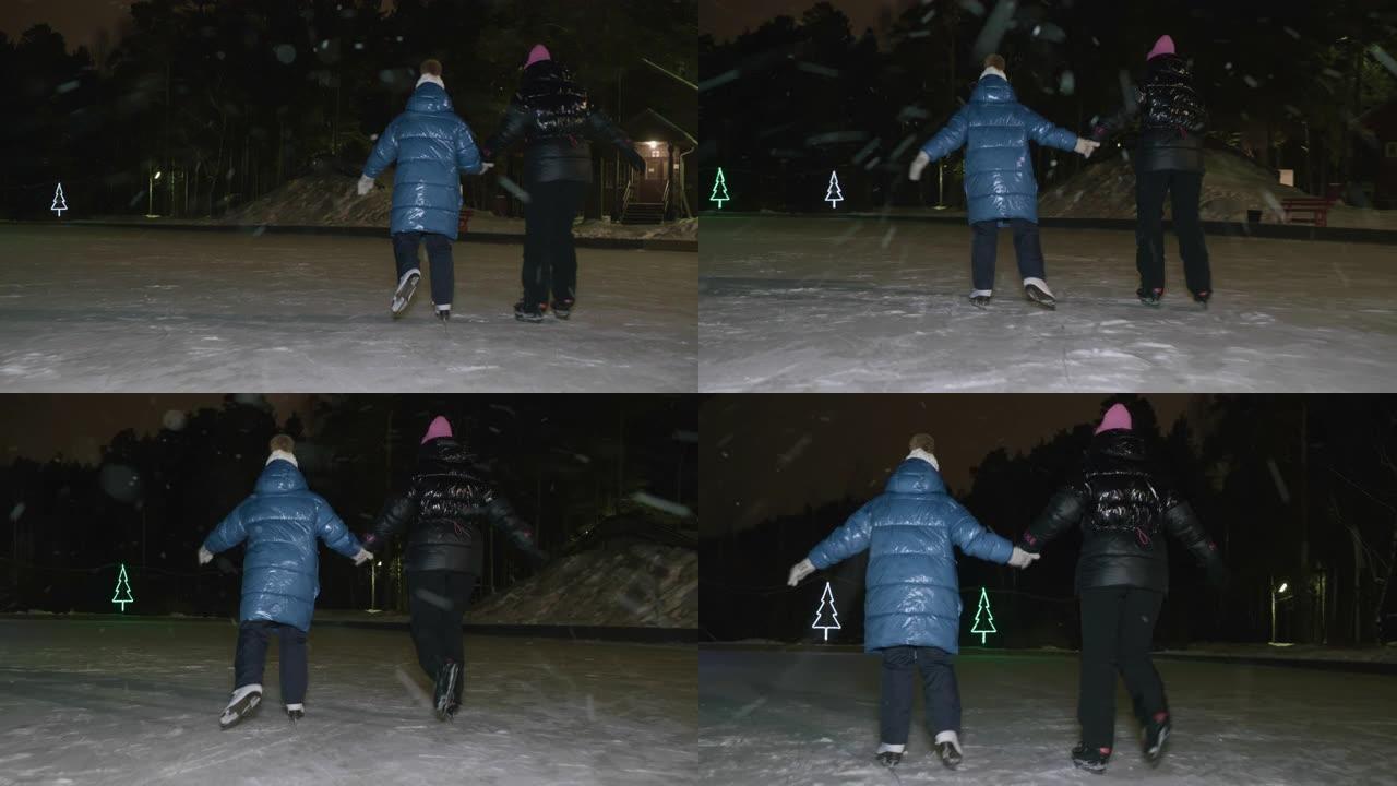 妈妈一起下雪时，女儿在冬季公园的夜间溜冰场上滑冰。母亲和少女在户外冬季溜冰场上骑着冰鞋时手牵手。
