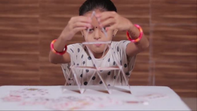 年轻的女孩孩子忙于在家中用纸牌屋建造金字塔-针对小学生的专注或集中运动游戏的概念