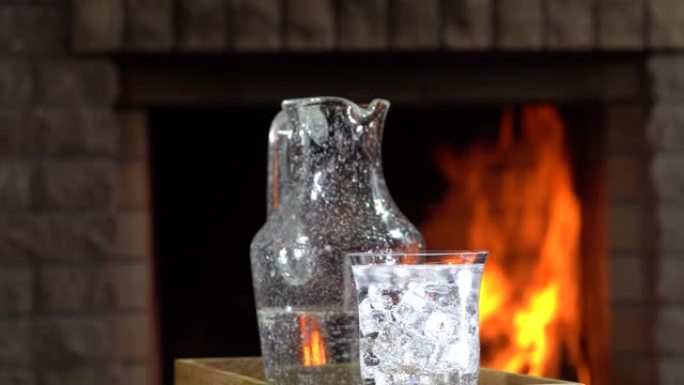 水罐和一杯装有冰的矿泉水在燃烧的壁炉前的桌子上旋转。