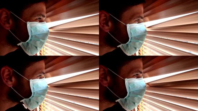 一个戴着医用口罩的年轻帅哥透过百叶窗看。一个戴着医用口罩的年轻人透过窗户看着自己的隔离。