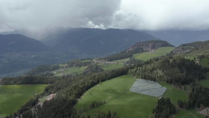 意大利山区绿色山坡上的太阳能电池农场的鸟瞰图，特伦蒂诺，山谷上的巨大云层，定居点房屋的屋顶，绿色的草