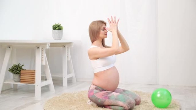 一位年轻漂亮的怀孕白人妇女坐在房子的柔软地毯上。他从事健身和锻炼。运动服。