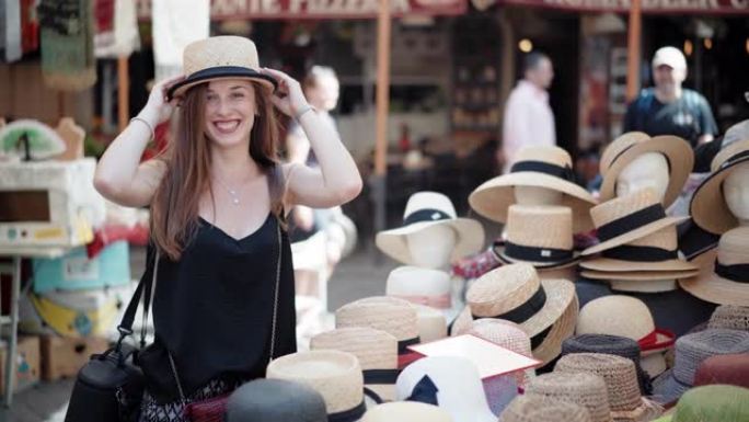 时尚的女孩在当地工艺品市场上试戴巴拿马帽子，看着镜子。市场柜台充满了不同类型和风格的头具，丰富多彩的