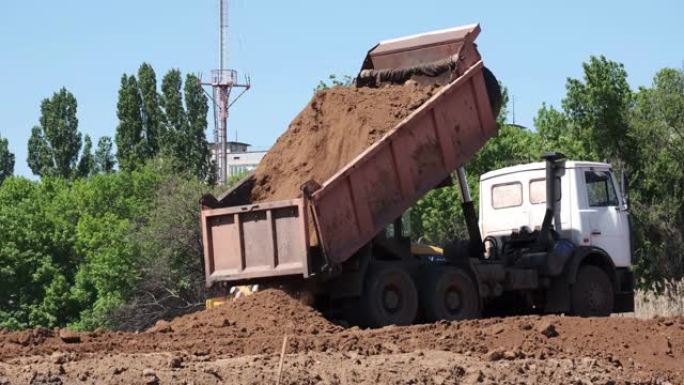 自卸车在地面上卸土，用于公路建设。重型工业机器建设一条新路。