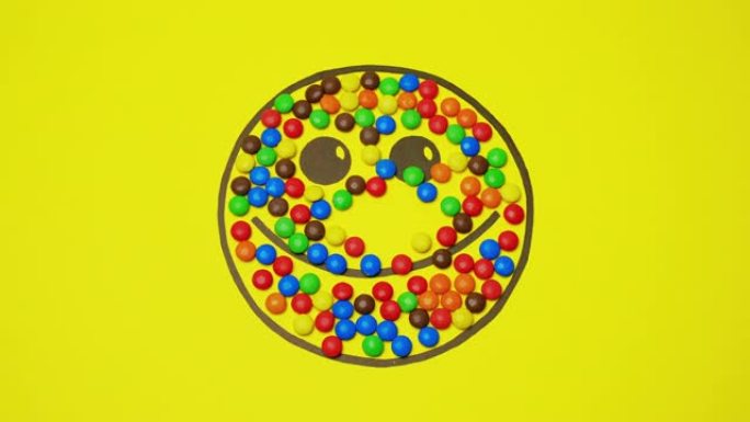 黄色背景上的笑脸充满了彩色糖果。圆形糖果远离图片。