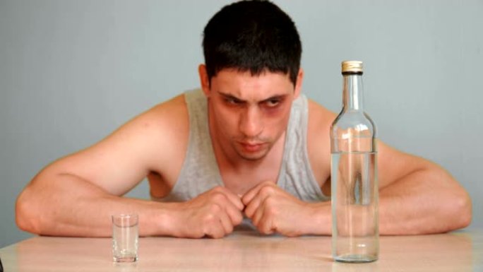 擦伤眼睛的年轻人正在酗酒。男人喝醉了，坐在家里的桌子上喝了一瓶酒精饮料。试图戒掉习惯。酒精成瘾的问题