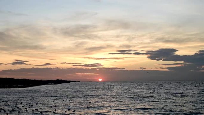 日落和云朵在美丽的海面上的时光倒流，海鸥在黄昏时飞过