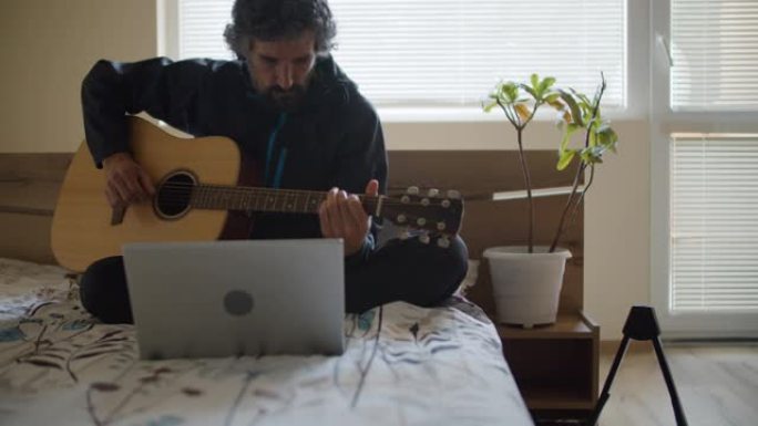 新型冠状病毒肺炎大流行期间在家工作的音乐家。自由职业者带着笔记本电脑和吉他在卧室里工作。活跃的老年人