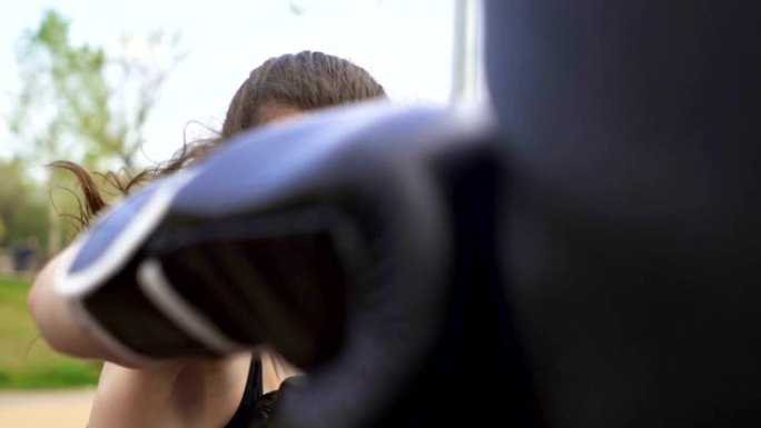 慢动作。在街头城市训练场用出气筒进行严肃的女拳击手训练。稳打，脸特写。自卫队。