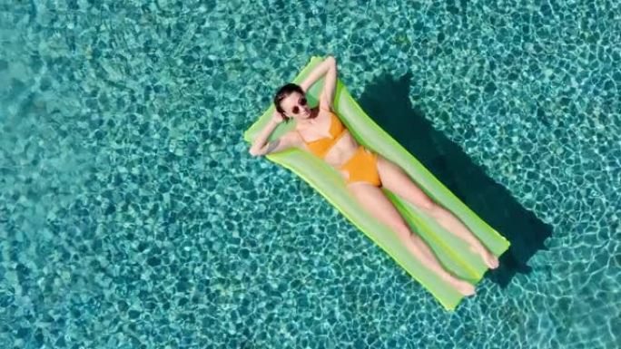性感的女人休息和日光浴在绿色的浮在游泳池，俯视图鸟瞰图。年轻女人在一个黄色的比基尼泳装漂浮在一个充气