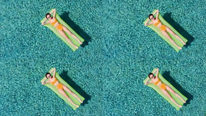 性感的女人休息和日光浴在绿色的浮在游泳池，俯视图鸟瞰图。年轻女人在一个黄色的比基尼泳装漂浮在一个充气