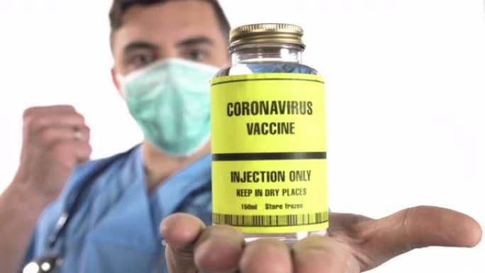 年轻的男性医生，听诊器拿着冠状病毒的疫苗瓶，在白色背景上显示OK标志