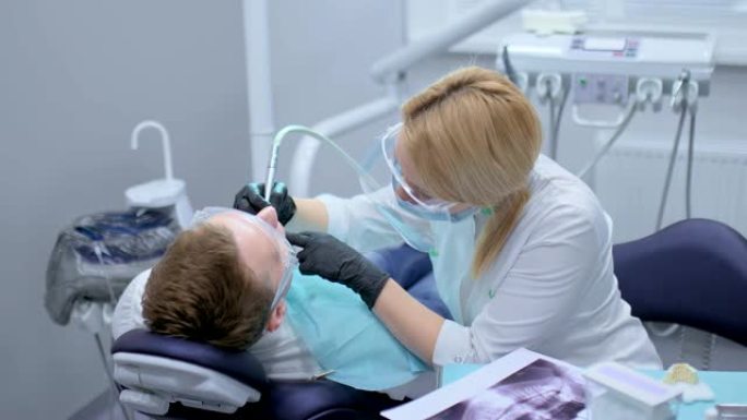 牙医戴着黑色无菌手套在患者的口腔中钻出一颗牙齿。牙科诊所用现代设备治疗龋齿。