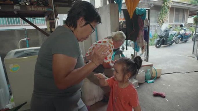 亚洲老妇为孙子们的拥抱挠着背，在屋子里快乐地玩耍。在家工作。