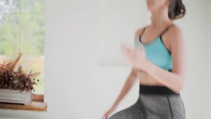 年轻健康的黑发女孩穿着蓝色上衣，紧身裤在明亮的房间里锻炼。在家做运动健身训练