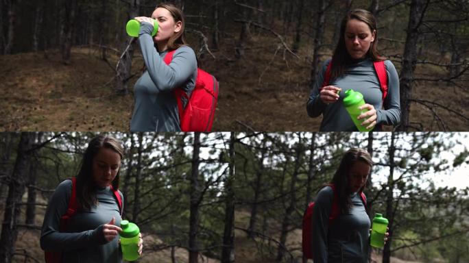 疲惫的健身女子早上在森林里徒步旅行后喝水