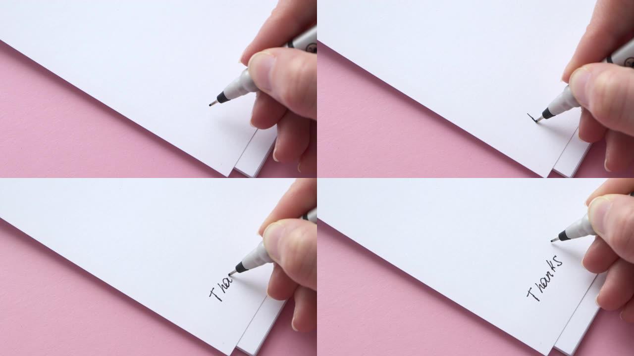 在白色记事本纸上写下感谢。粉红色背景上的女性手握笔笔记或字母，特写