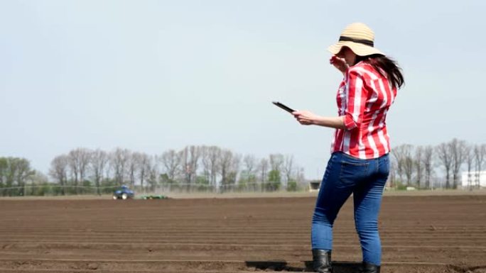 女农民，农艺师站在田间特殊的土壤行之间。她使用片剂测试了中耕者种植马铃薯的质量。现代农业种植。春天阳