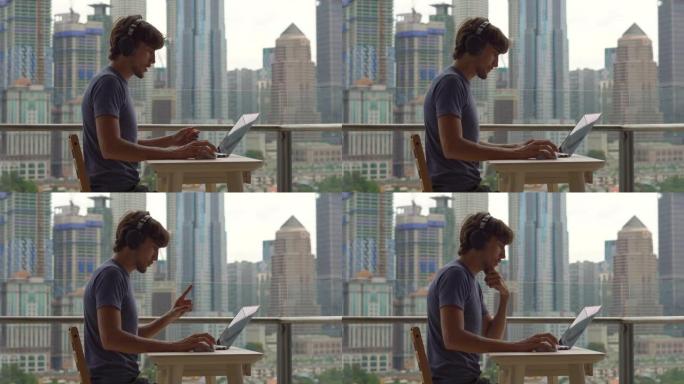 年轻的自由职业者在阳台上的笔记本电脑上工作，阳台上的背景是一个充满摩天大楼的市中心。自由职业it专家