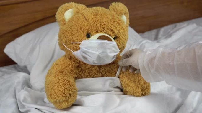 泰迪熊用水银温度计测量温度。医生拿温度计。熊躺在床上，戴着医用口罩。