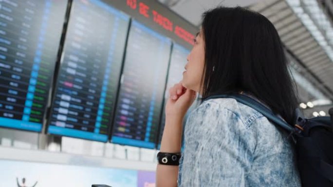 亚洲旅行者妇女在机场的计时板上检查飞机的飞行