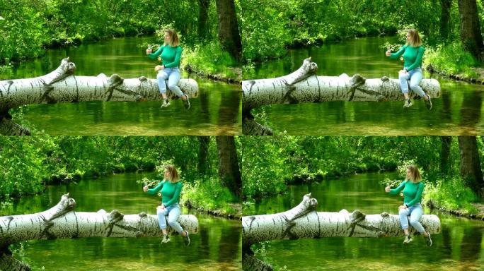 美丽的年轻女子在森林丛中河上的原木上自拍