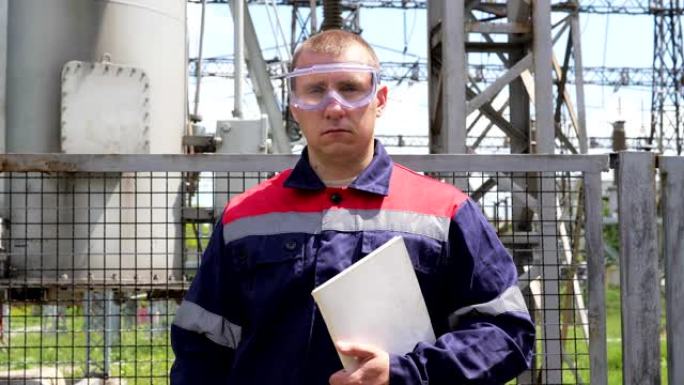 在发电站附近，戴着头盔的手拿着平板电脑的男性工程师的肖像。电力工程