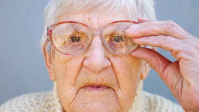 戴眼镜沉思的老太太肖像。关闭女性养老金领取者的皱纹脸，看着相机并调整眼镜。奶奶悲伤的面部表情。成熟女