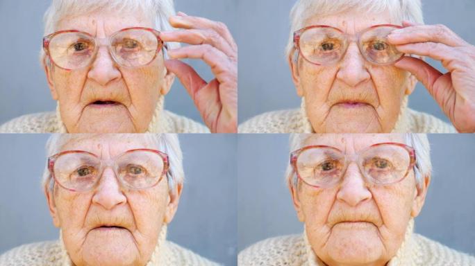 戴眼镜沉思的老太太肖像。关闭女性养老金领取者的皱纹脸，看着相机并调整眼镜。奶奶悲伤的面部表情。成熟女