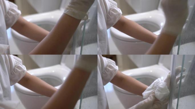 女性手在家里用弹性白手套擦拭浴室玻璃门，玻璃表面材料，消毒湿巾，防止冠状病毒covid19，家庭清洁