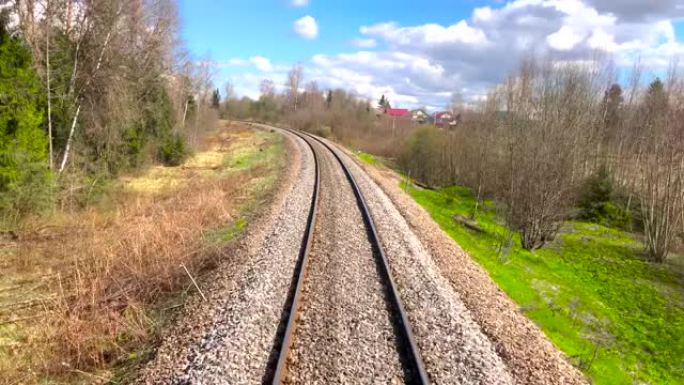 火车行驶时的铁路景色，在春季晴朗的天气中，在林木之间的村庄房屋附近的弯道上行驶