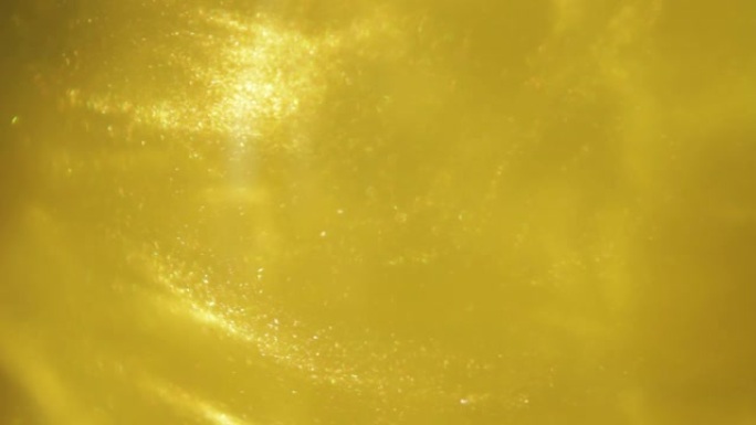 金色墨水灰尘漂浮在液体中。金色闪光的沙子在水中旋转