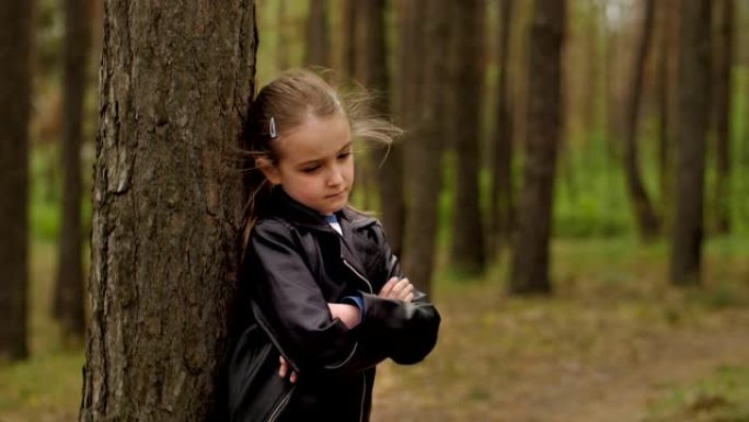 一个悲伤愤怒的小女孩站在森林里的一棵树前