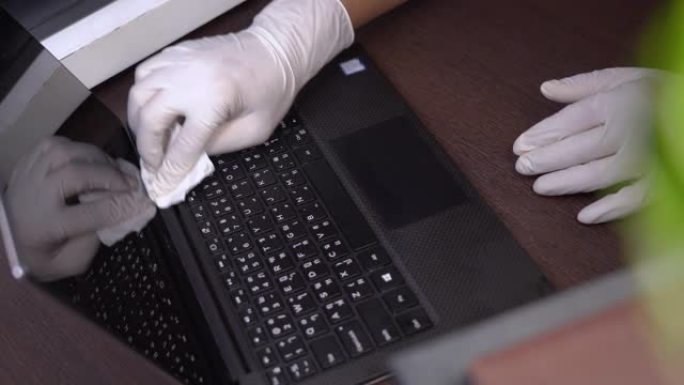 手在白手套清洁黑色电脑笔记本电脑，消毒湿巾，电子硬件设备护理，冠状病毒新冠病毒，杀灭细菌，医疗保健，