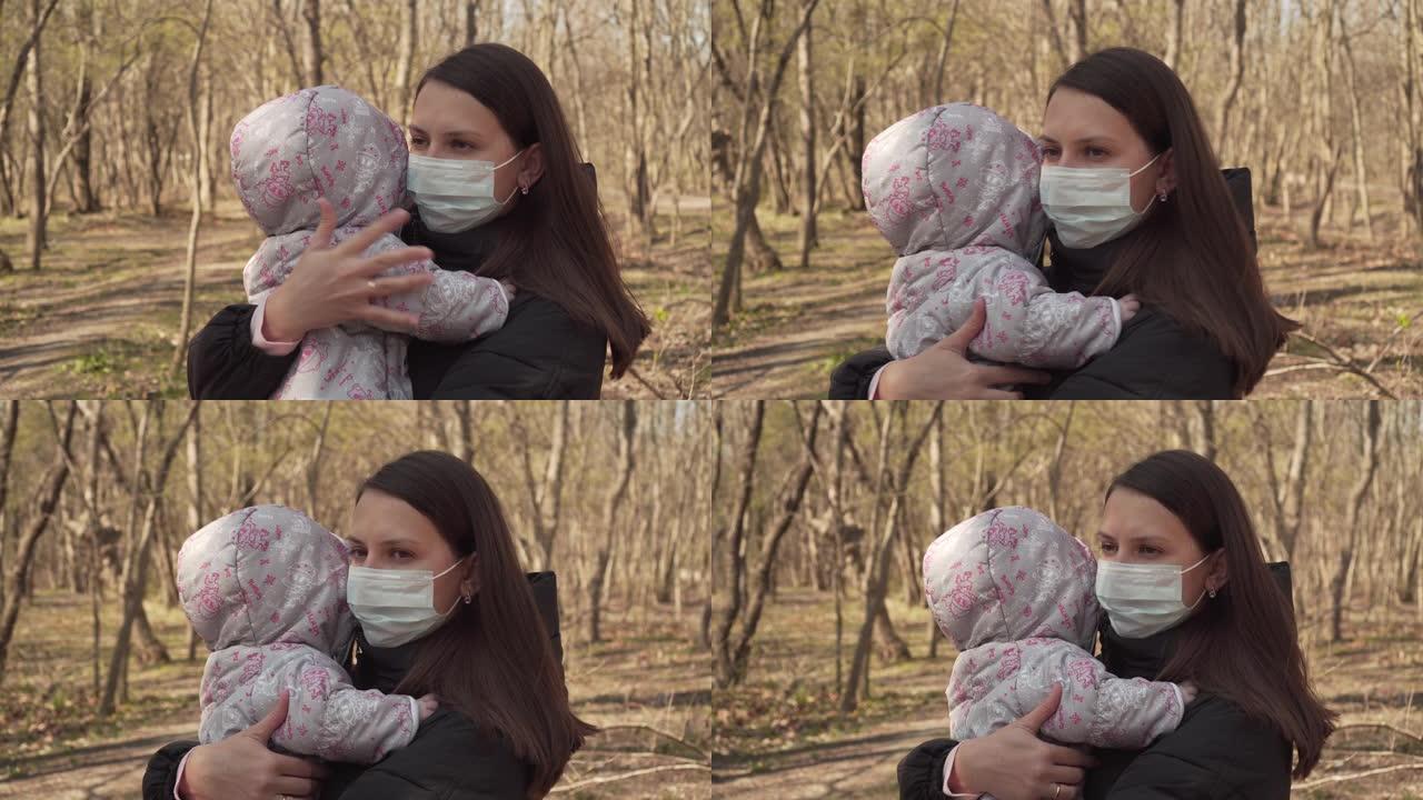 戴着防护面具的妈妈带着婴儿在公园散步。冠状病毒大流行条件。带着孩子的女人的严肃表情