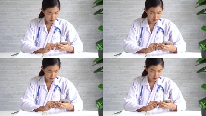 年轻的亚洲女医生在医院使用手机。医护人员在办公室滚动和键入短信