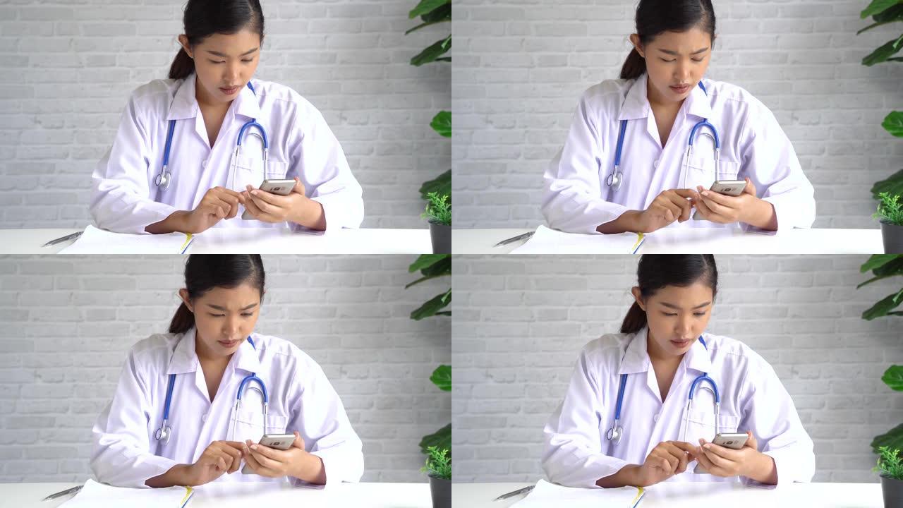 年轻的亚洲女医生在医院使用手机。医护人员在办公室滚动和键入短信