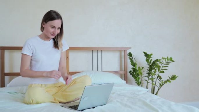 女人使用笔记本电脑，坐在床上，庆祝成功，在线彩票中奖，阅读好消息，在家卧室在社交网络中聊天