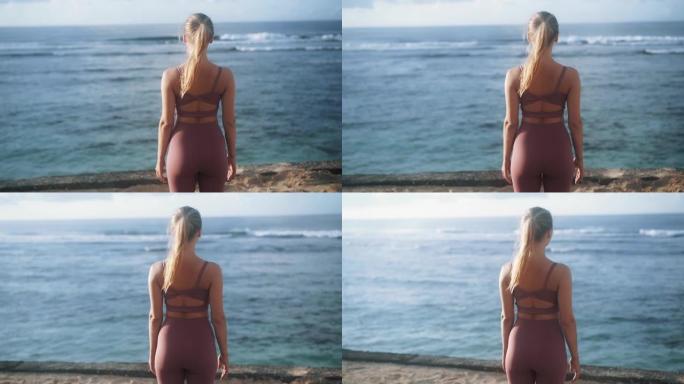 穿着运动服的女人的背面景色站在海滩上，看着海浪
