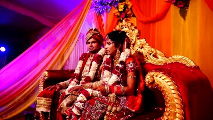 多莉拍摄的年轻印度婚礼夫妇坐在豪华沙发上，他们都在婚礼舞台上互相交谈