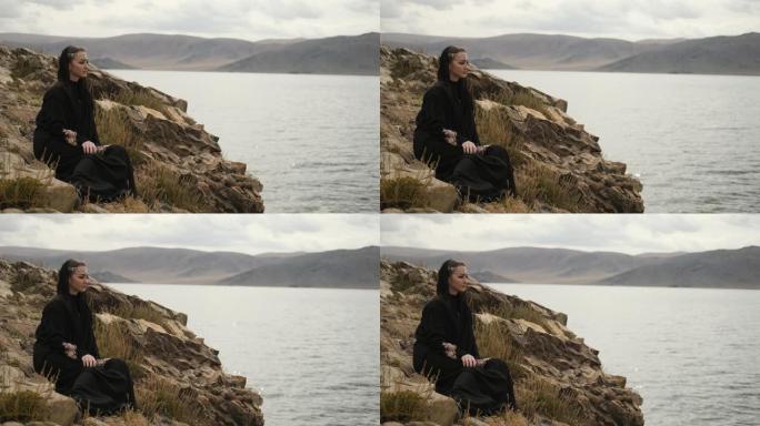 穿着黑色连衣裙的女人，坐在山顶的悬崖边