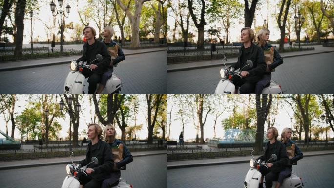 快乐的年轻时髦夫妇在旧城中心公园骑着一辆老式踏板车，带着杂货纸袋，跟踪镜头