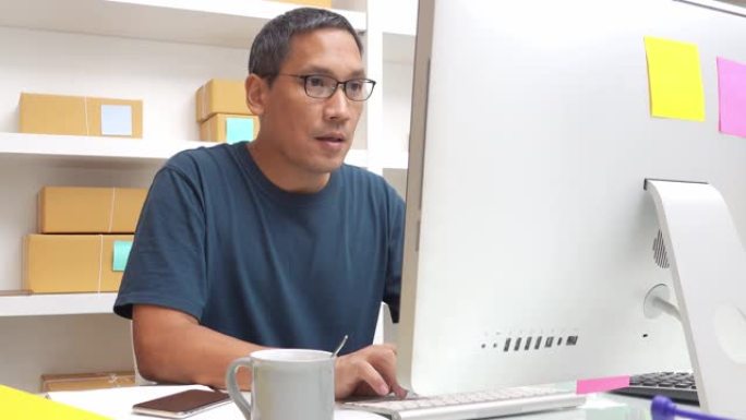 亚洲小商人在家用电脑工作，在线企业主用纸箱准备送到送货公司。